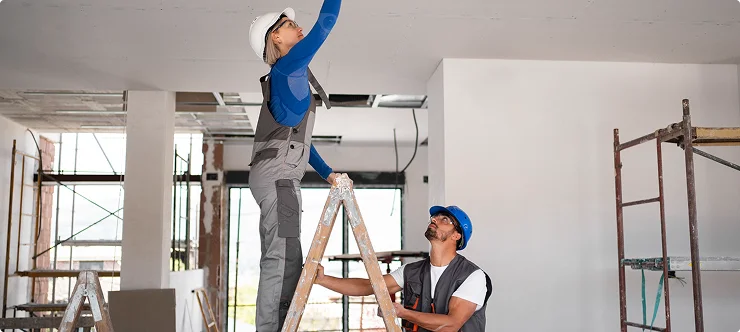 Two construction workers in hard hats working on ceiling during interior renovation