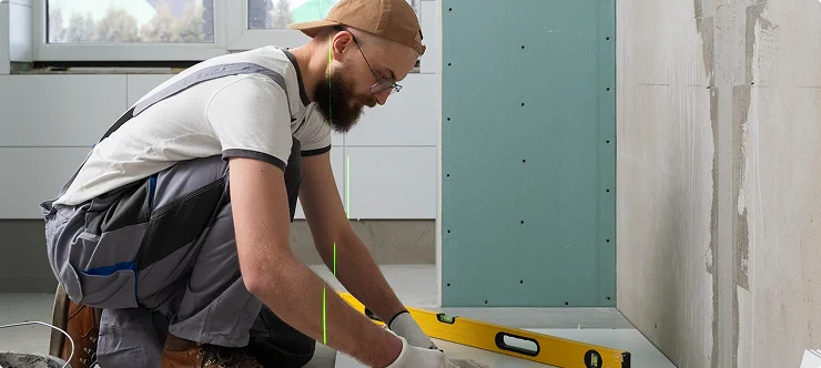Worker measuring floor level with spirit level during drywall installation