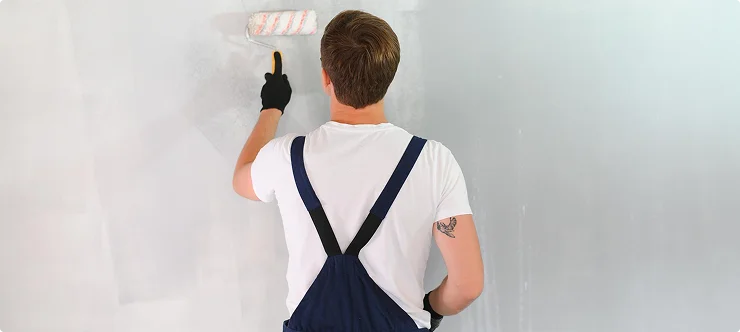 Painter in overalls applying paint to wall with roller