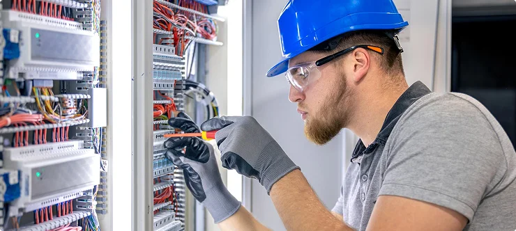 Electrician in hard hat wiring electrical control panel